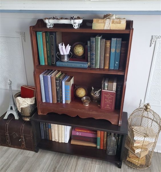 Twenty-dollar thrifted vintage bookcase styled with old books, miniature globes, decorative objects, a small Eiffel Tower, antique suitcase, and wire birdcage in a cozy home library.