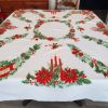 Vintage Christmas tablecloth measuring 52 x 42 inches, featuring red poinsettias, holly, candles, bells, ornaments, and decorative evergreen garlands on a white background.