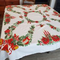 Vintage Christmas tablecloth measuring 52 x 42 inches, featuring red poinsettias, holly, candles, bells, ornaments, and decorative evergreen garlands on a white background.