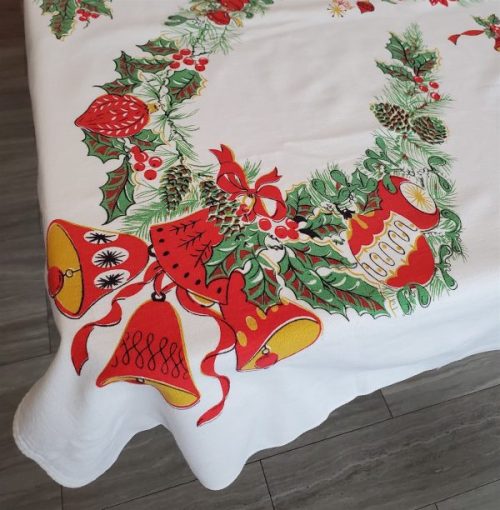 Vintage Christmas tablecloth measuring 52 x 42 inches, featuring red poinsettias, holly, candles, bells, ornaments, and decorative evergreen garlands on a white background.