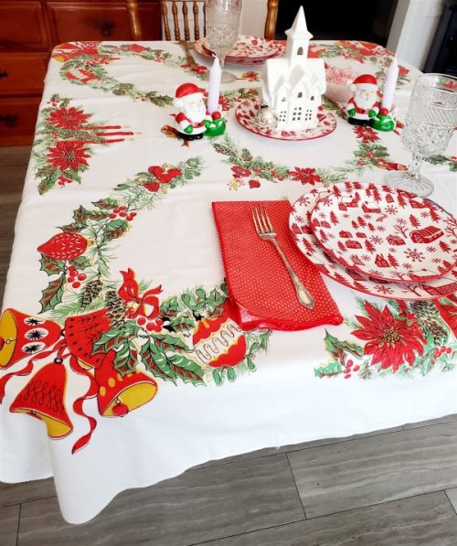 Vintage Christmas tablecloth measuring 52 x 42 inches, featuring red poinsettias, holly, candles, bells, ornaments, and decorative evergreen garlands on a white background.