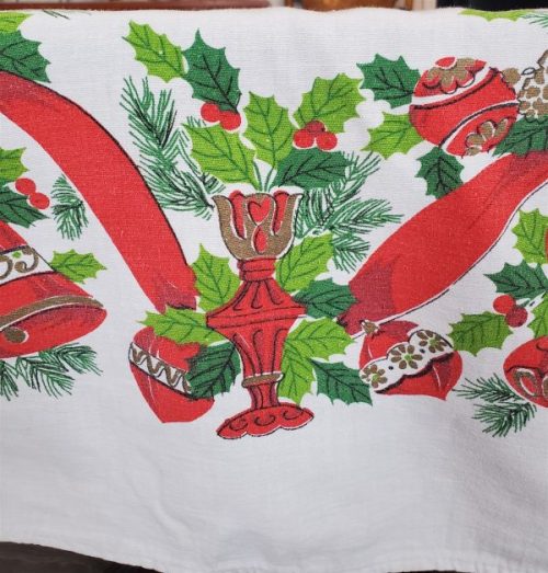 Close-up of vintage Christmas tablecloth showing holly, ornaments, bells, ribbon, and candy cane pattern.
