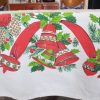 Close-up of vintage Christmas tablecloth showing holly, ornaments, bells, ribbon, and candy cane pattern.